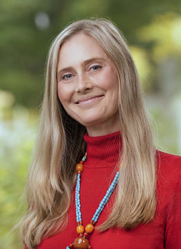 Woman with long blonde hair and red turtleneck with blue beaded necklace